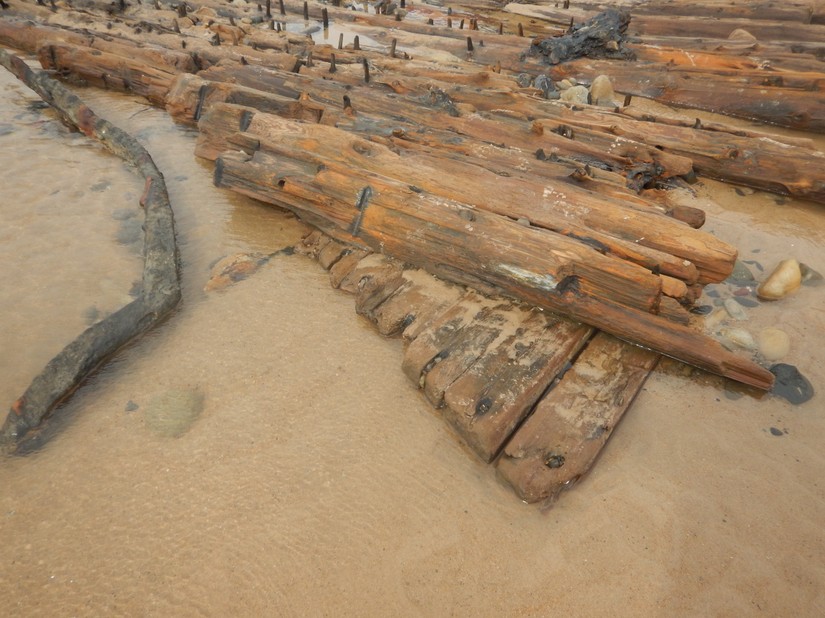 The ship's hull planking protude from underneath the frames